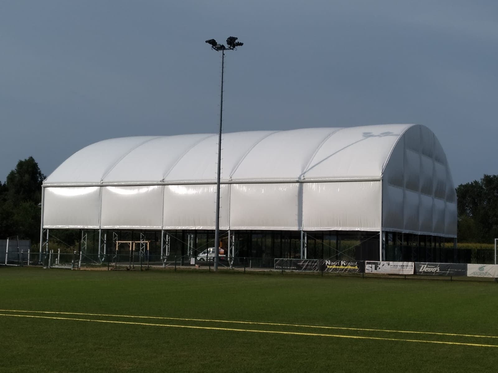 Large white fabric-covered sports structure on a green field with a tall light pole.