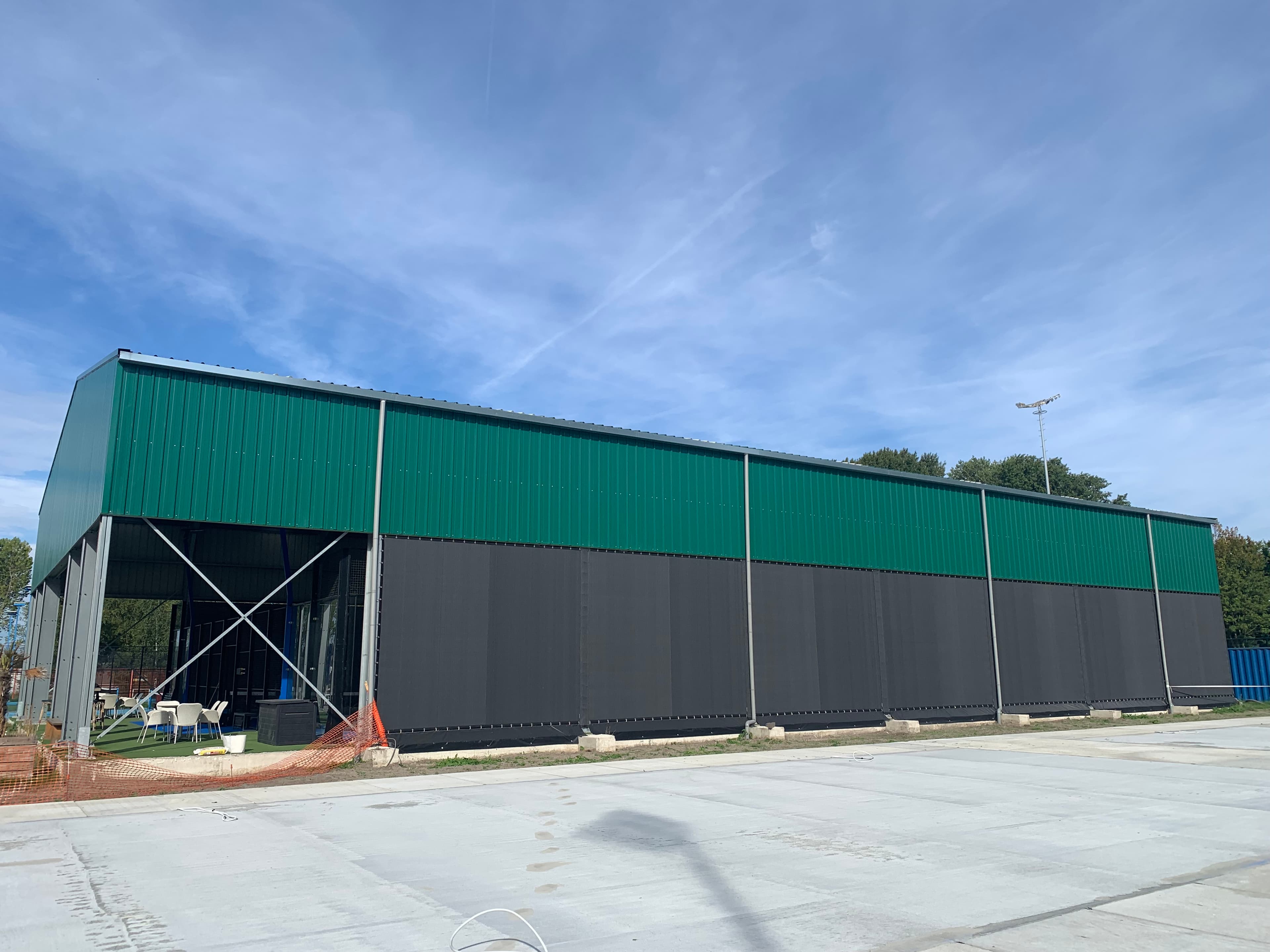 Modern green and black sports facility with an open side and large concrete foreground.