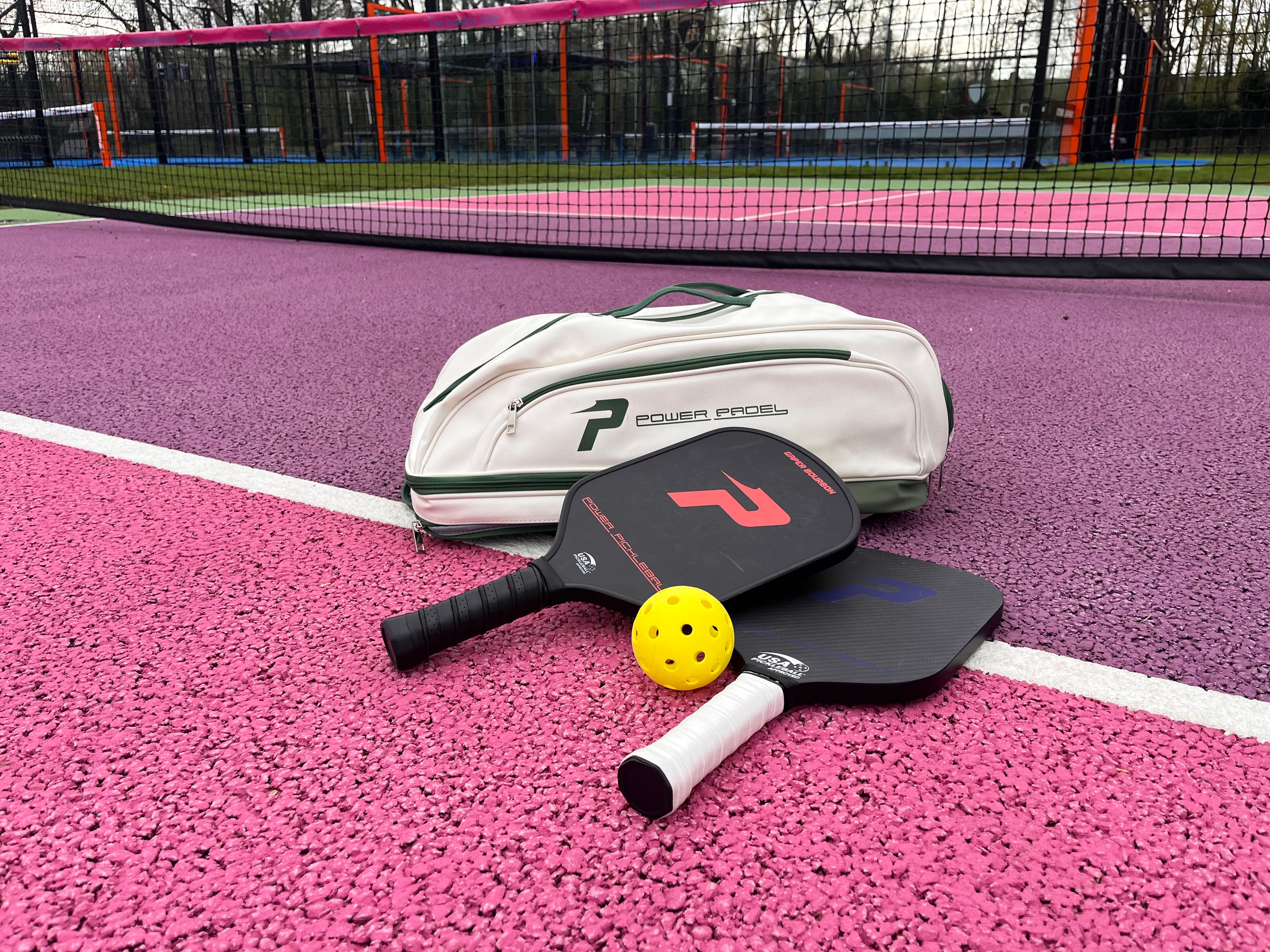 Pickleball paddles, a yellow ball, and a white bag on a pink and purple court.
