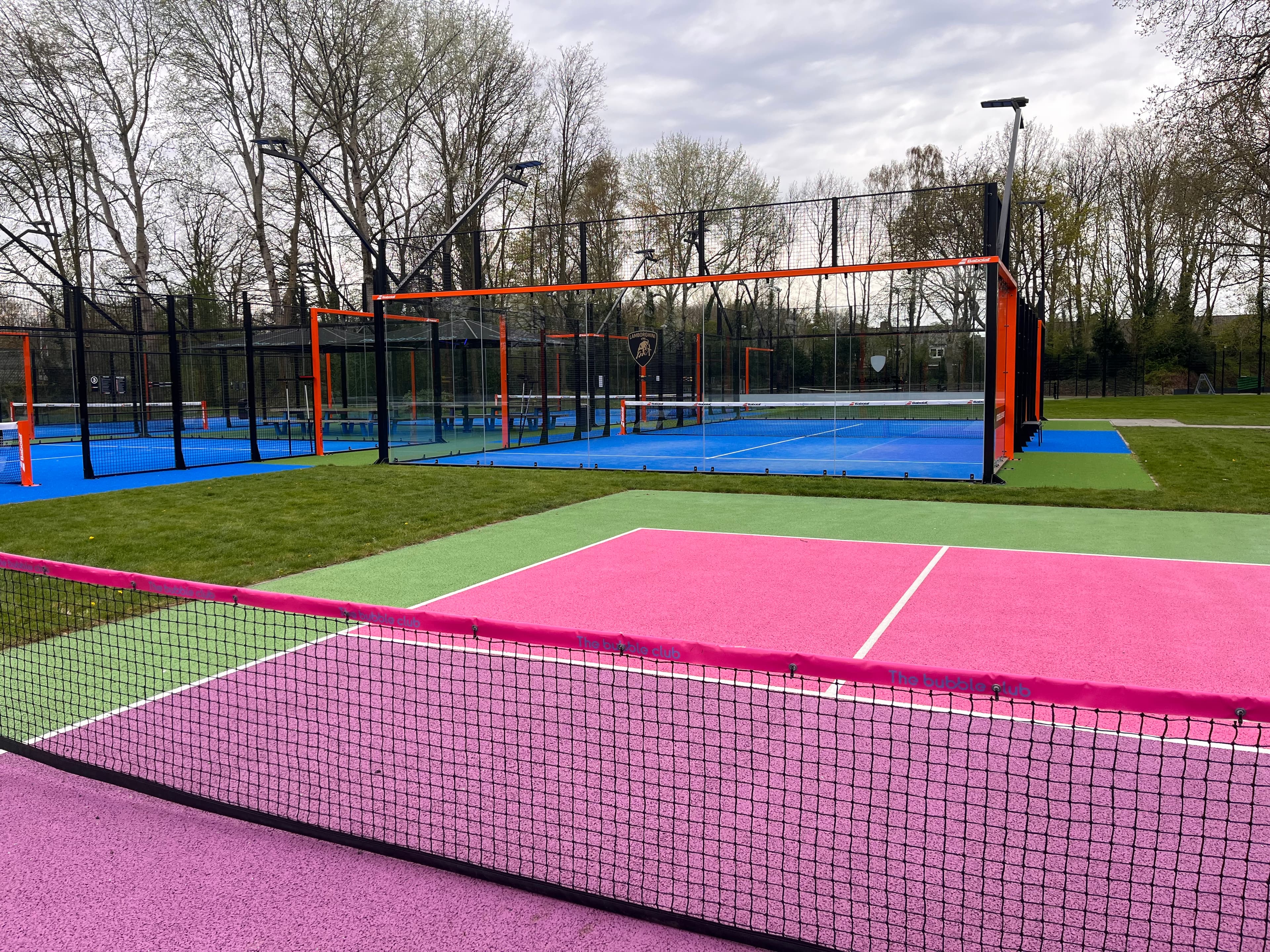 Pink and purple court in front of blue padel courts at an outdoor sports facility.