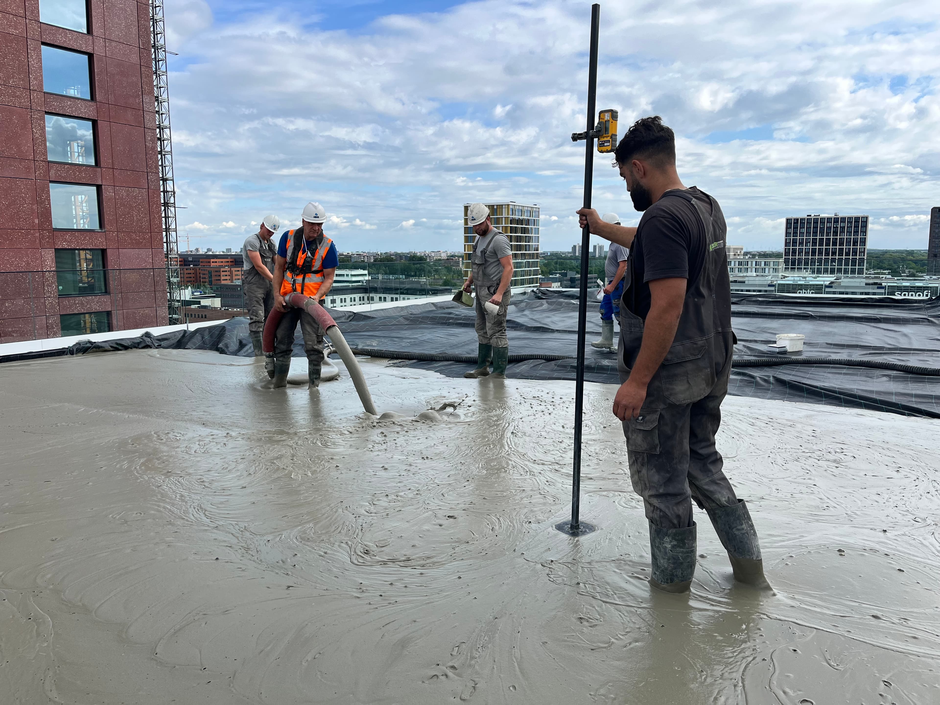 Construction workers pouring and leveling wet concrete on a rooftop overlooking a city skyline.