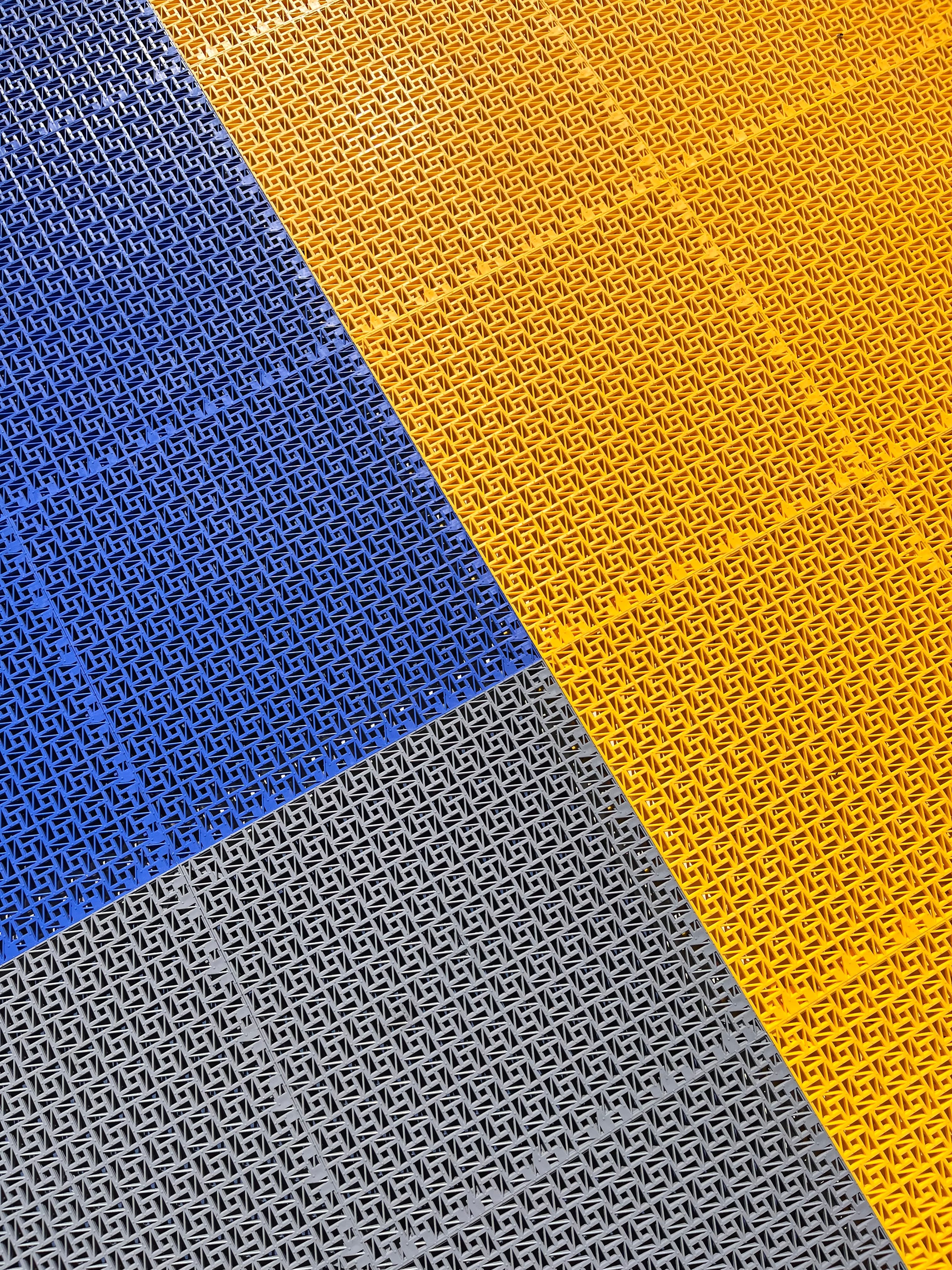 Interlocking plastic floor tiles with a geometric mesh pattern in yellow, blue, and grey sections.